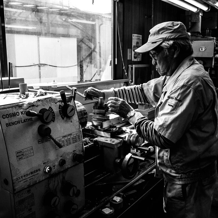 工房で旋盤を操作する職人、作業着姿でブラシ部品を加工する様子