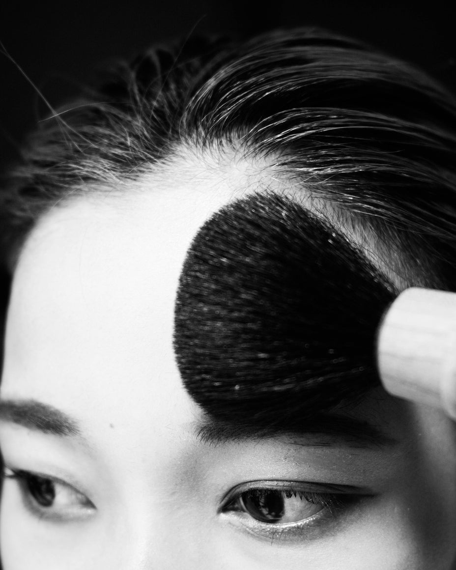 H PRODUCTのブラシを額に当てる女性の顔、髪の流れが美しいモノクロ写真