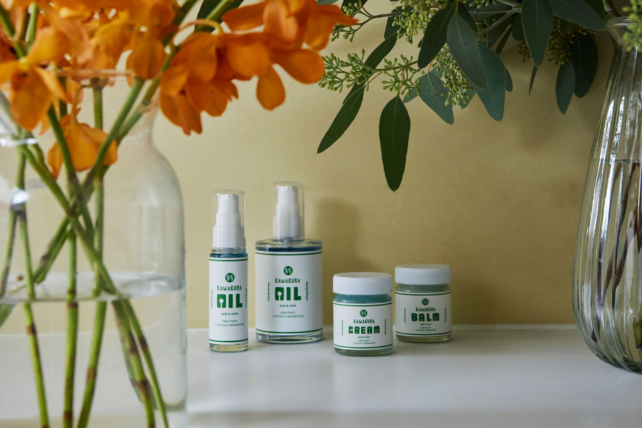 オレンジの花と緑の植物に囲まれたH PRODUCTのヘアケア製品4点