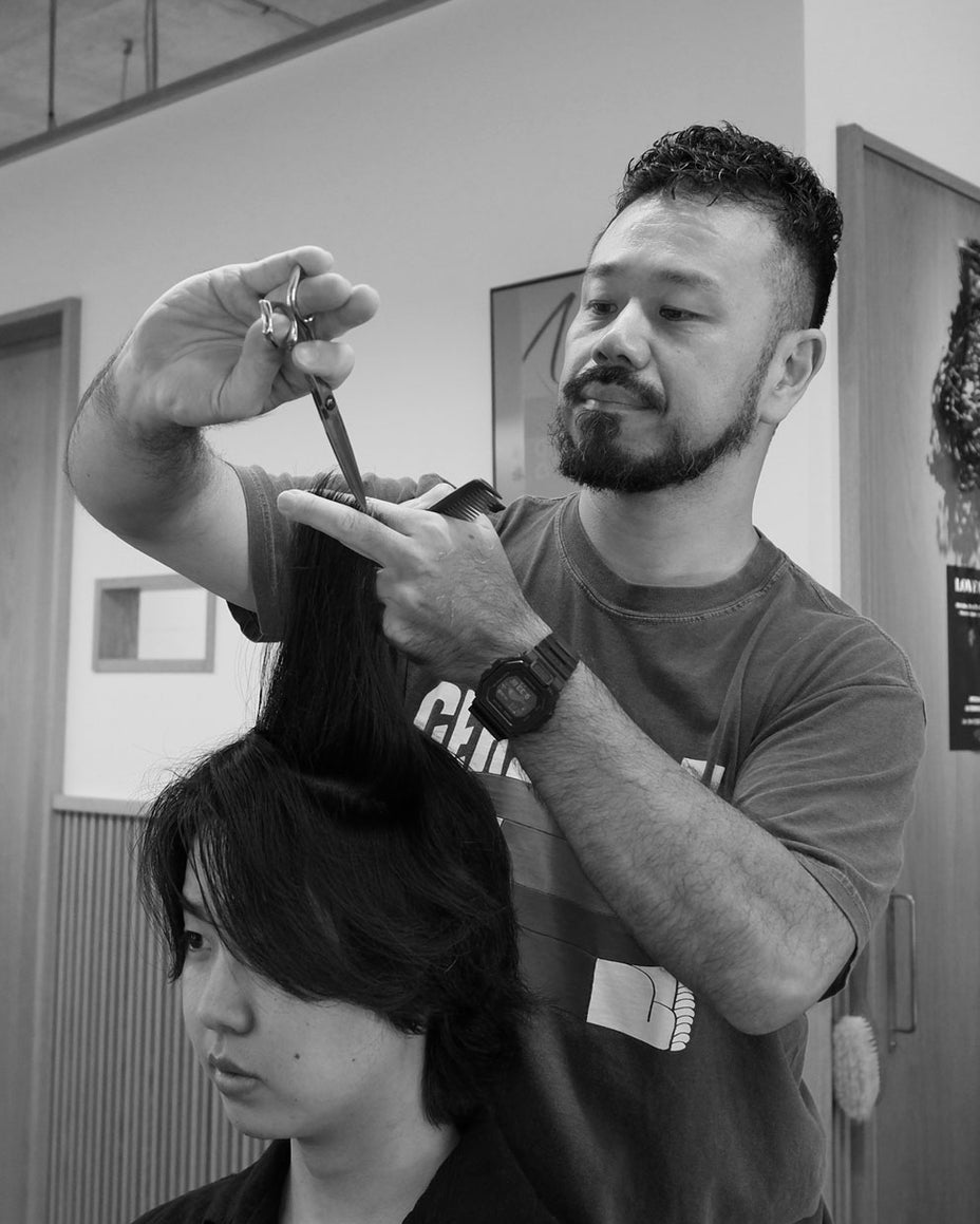 美容師が客の髪をハサミでカット、集中した表情で施術する様子のモノクロ写真